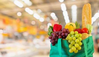 Fresh fruits and vegetables in reusable green shopping bag with supermarket grocery store blurred defocused background with bokeh light photo