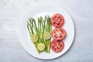 Healthy food asparagus grill with lemon and tomato in plate on white wood background top view. photo