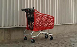 Empty red shopping on industrial wall background. Shop trolley at supermarket. Sale, discount, shopaholism, black friday, economy concept. Consumer society trend. Online Shopping Concept. photo