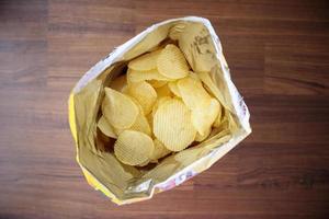 Potato chips in open snack bag close up on table floor photo