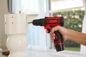 man assembling white table furniture at home using cordless screwdriver photo