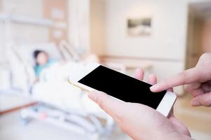 Female hand holding mobile smart phone with blurred hospital room with patient background photo