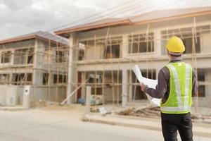 young professional engineer in protective helmet and blueprints paper at the house building construction site photo