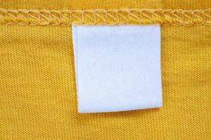 White blank clothing tag label on new yellow shirt background photo