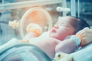 Newborn baby girl inside incubator in hospital post delivery room photo