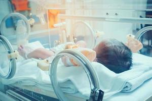 Newborn baby girl inside incubator in hospital post delivery room photo