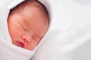 Cute newborn asian baby girl sleeping on white fabric photo