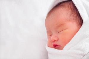 Cute newborn asian baby girl sleeping on white fabric photo