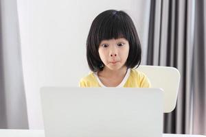 little asian girl student study online using laptop computer at home photo