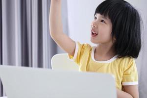 little asian girl student study online using laptop computer at home photo