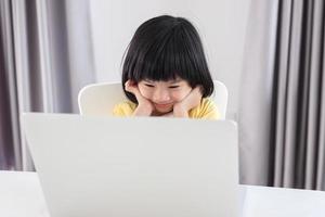 little asian girl student study online using laptop computer at home photo