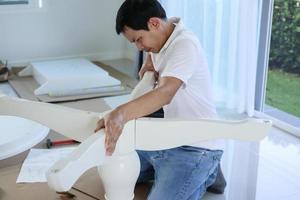 Asian man assembling white table furniture at home photo