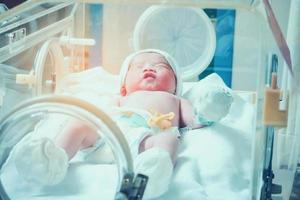 Newborn baby girl inside incubator in hospital post delivery room photo