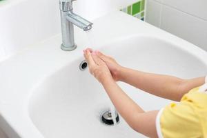 Little girl washing hand under faucet with water photo