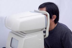 Young handsome asian man take eye exam with optical eye test machine photo