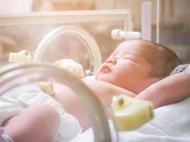 Newborn baby girl inside incubator in hospital post delivery room photo