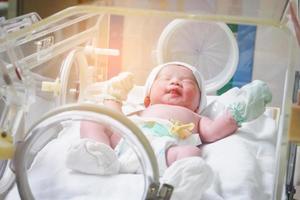 Newborn baby girl inside incubator in hospital post delivery room photo