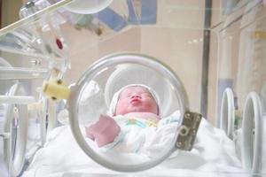 Newborn baby girl inside incubator in hospital post delivery room photo