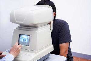 joven y apuesto hombre asiático tome un examen de la vista con una máquina de prueba ocular óptica foto
