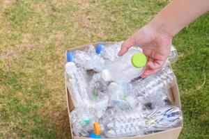 sostenga con la mano y coloque botellas de plástico en una caja de basura de reciclaje marrón foto