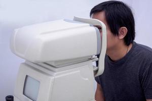 Young handsome asian man take eye exam with optical eye test machine photo