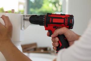 man assembling white table furniture at home using cordless screwdriver photo