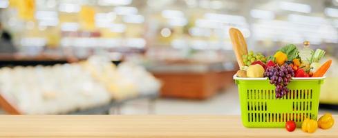 Shopping basket filled with fruits and vegetables on wood table with supermarket grocery store blurred defocused background with bokeh light photo