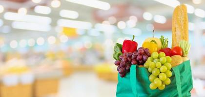 Fresh fruits and vegetables in reusable green shopping bag with supermarket grocery store blurred defocused background with bokeh light photo