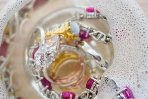 cleaning vintage jewelry diamond ring and bracelet in glass on wood table background photo