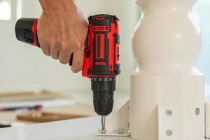 man assembling white table furniture at home using cordless screwdriver photo