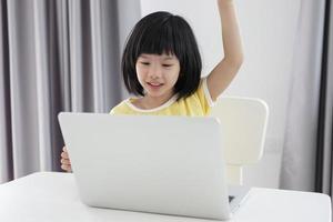 little asian girl student study online using laptop computer at home photo