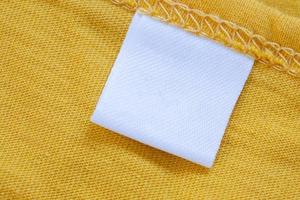 White blank clothing tag label on new yellow shirt background photo