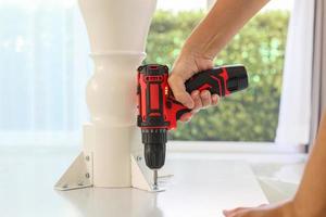 man assembling white table furniture at home using cordless screwdriver photo