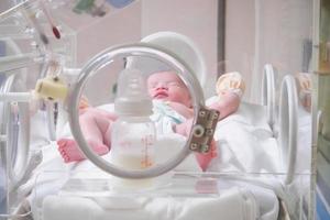 Newborn baby girl inside incubator in hospital post delivery room photo