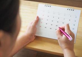 calendar page with female hand holding pen on desk table photo