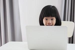 una pequeña estudiante asiática estudia en línea usando una computadora portátil en casa foto