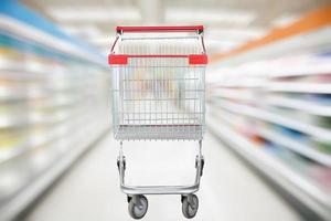 Supermarket aisle blur defocused background with empty red shopping cart photo