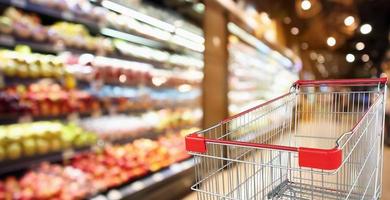 supermarket grocery store with fruit and vegetable shelves interior defocused background with empty red shopping cart photo