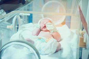 Newborn baby girl inside incubator in hospital post delivery room photo