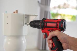 man assembling white table furniture at home using cordless screwdriver photo