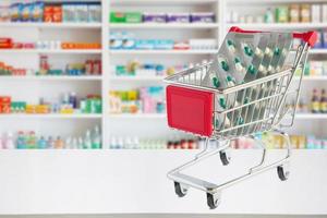 Cápsula de píldoras de medicina en el carrito de compras en el mostrador de la farmacia con estantes de farmacia borrosos fondo desenfocado foto