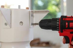 man assembling white table furniture at home using cordless screwdriver photo