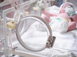 Newborn baby girl inside incubator in hospital post delivery room photo