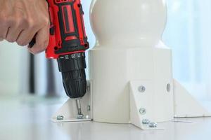 man assembling white table furniture at home using cordless screwdriver photo