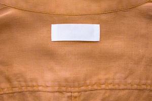 White blank clothing tag label on brown linen shirt fabric texture background photo