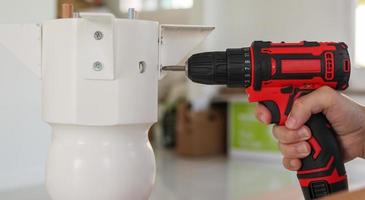 man assembling white table furniture at home using cordless screwdriver photo