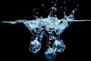 cubos de hielo en agua con burbujas sobre fondo negro foto