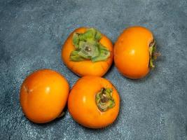 Persimmons on a black background. Persimmon varieties Chamomile. still life. Big ripe tasty fruits on the table. View from above photo