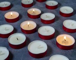 Short candles are burning against a dark background. Lots of small candles. Not all candles are lit. photo