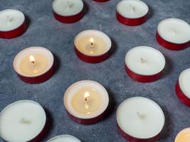 Short candles are burning against a dark background. Lots of small candles. Not all candles are lit. photo